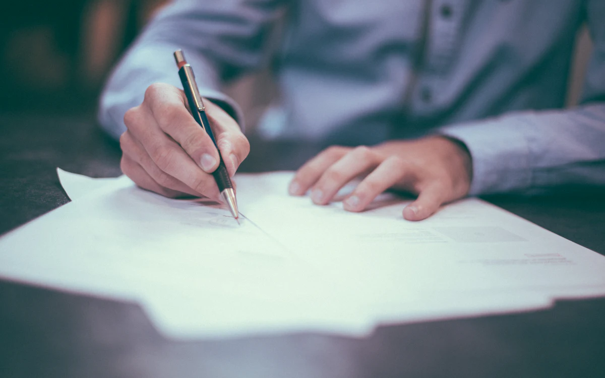 Una persona revisa y firma documentos en papel sobre un escritorio