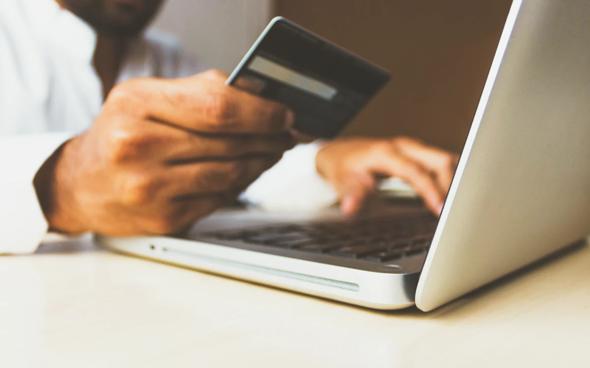 Persona sentada frente a una laptop con una tarjeta bancaria en la mano
