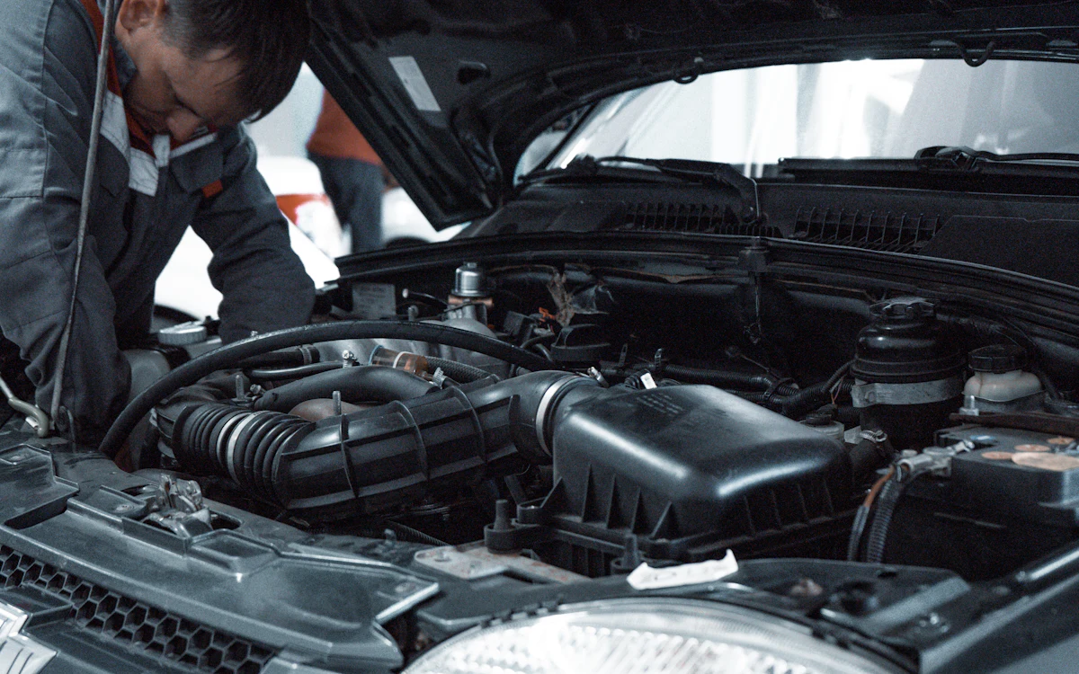 Un mecánico con uniforme revisa el motor de un auto con el cofre abierto