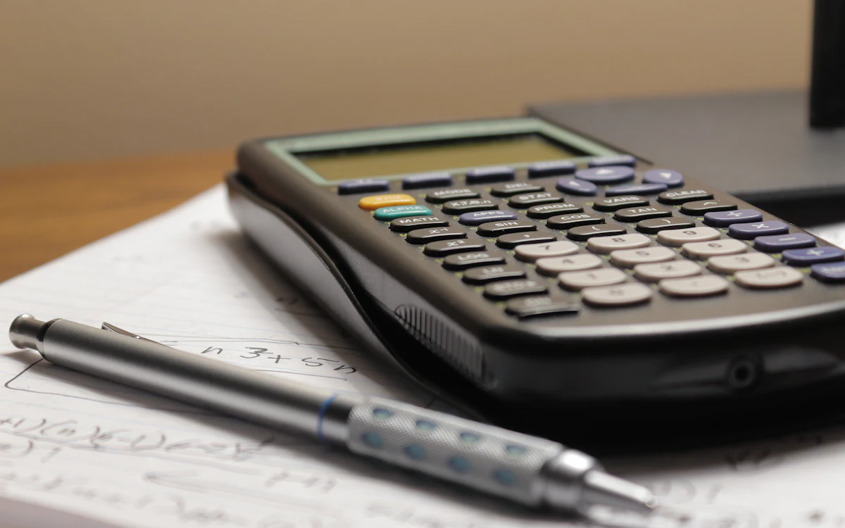 Una calculadora y una pluma sobre una hoja con operaciones escritas a mano