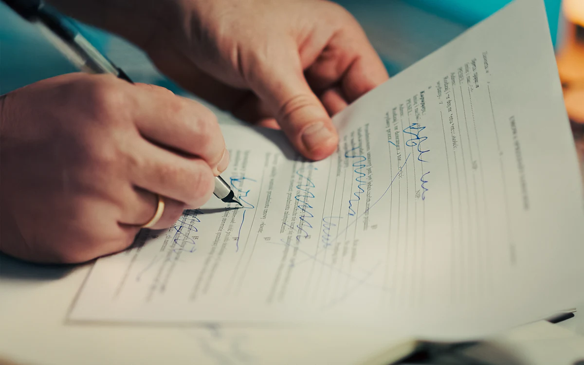 Una persona firma a mano un documento impreso sobre una mesa