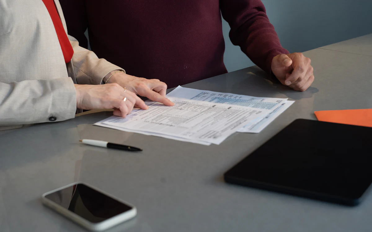 Dos personas revisan papeles impresos sobre una mesa, junto a un celular y una tableta