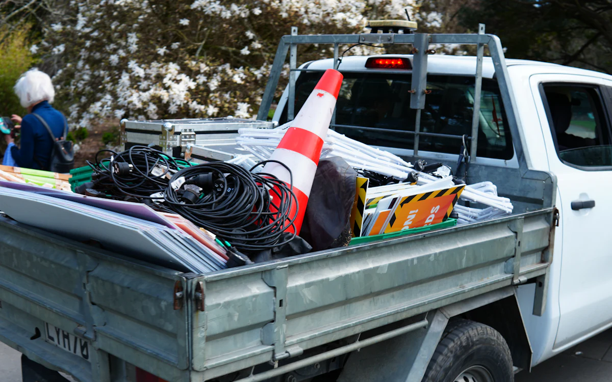 Caja de una pick-up blanca cargada con cables, un cono y señales de obra